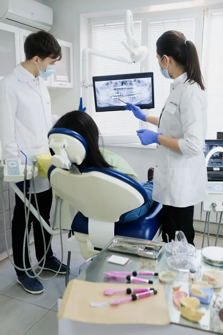 Dos odontólogos revisan una radiografía en el monitor junto a un paciente en el sillón